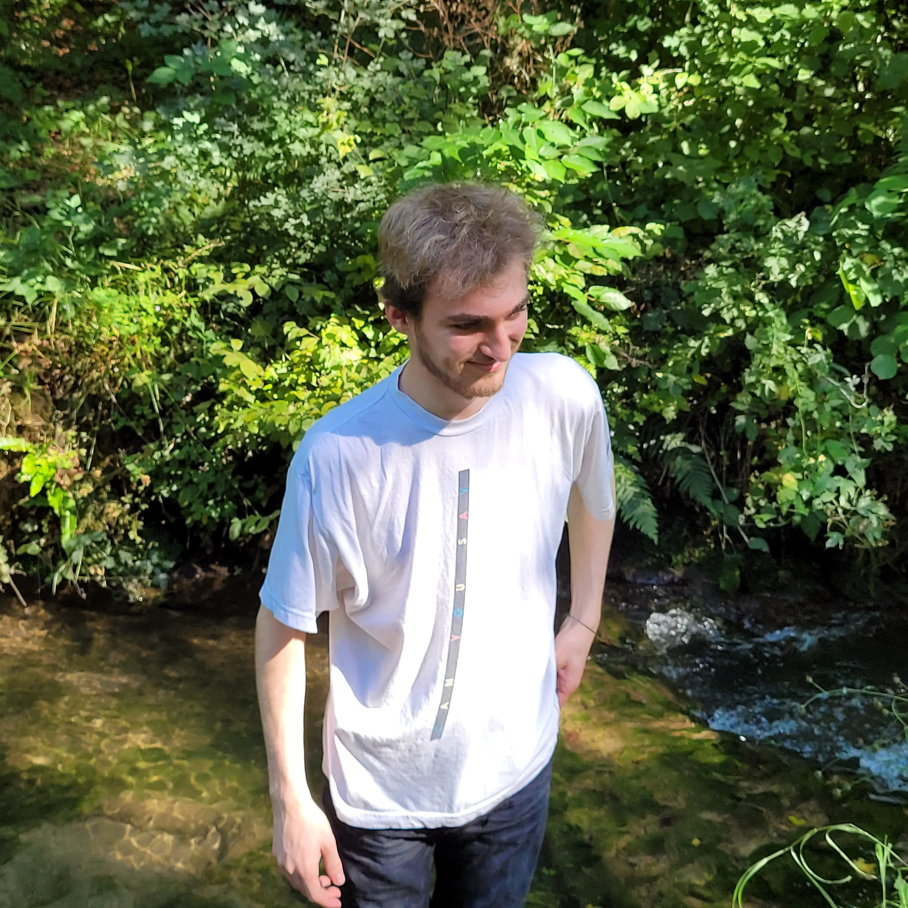 Un homme blond, en t-shirt blanc, avec des plantes en arrière-plan